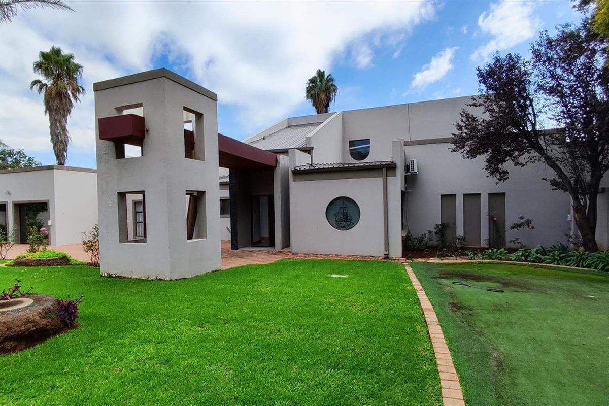 A view of the rear exterior of the property, featuring a modern architectural design, a well-maintained lawn, and a paved patio area.