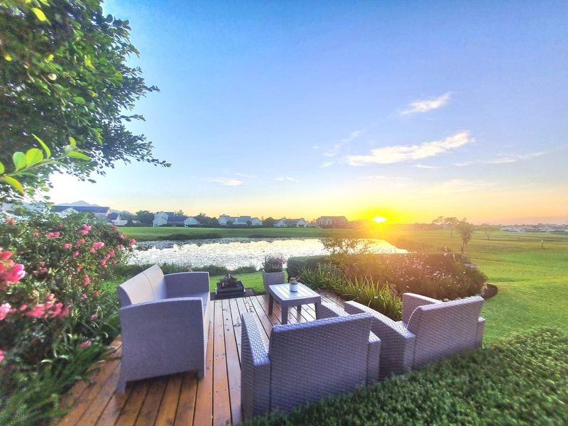 A scenic outdoor timber deck overlooking a tranquil pond and landscaped estate grounds at sunset.