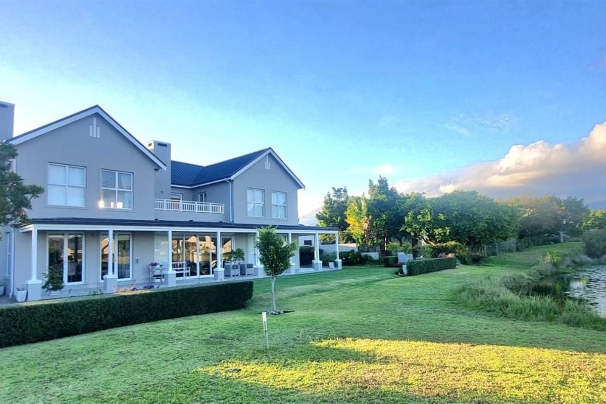 A spacious double-story residence featuring a covered patio, manicured lawn, and scenic views overlooking a tranquil pond.