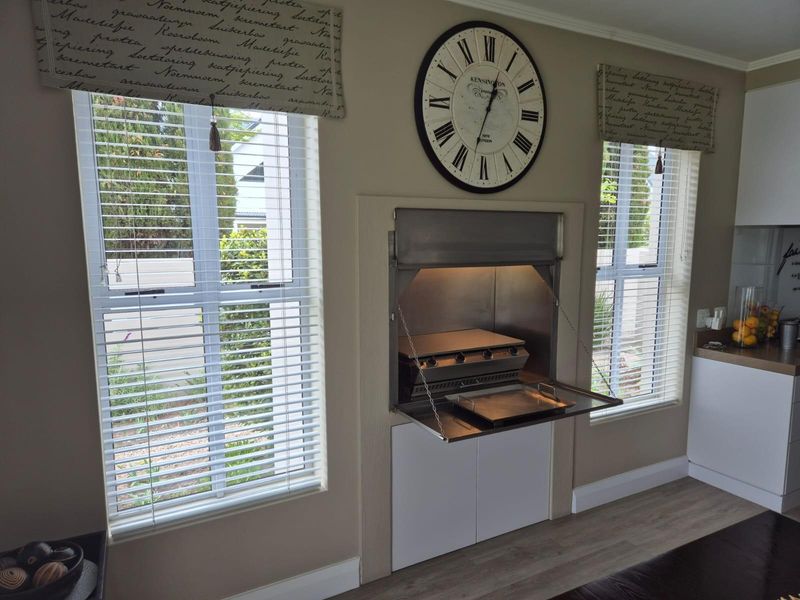Indoor living area featuring a built-in stainless steel braai unit with integrated cabinetry and large windows with fitted blinds.