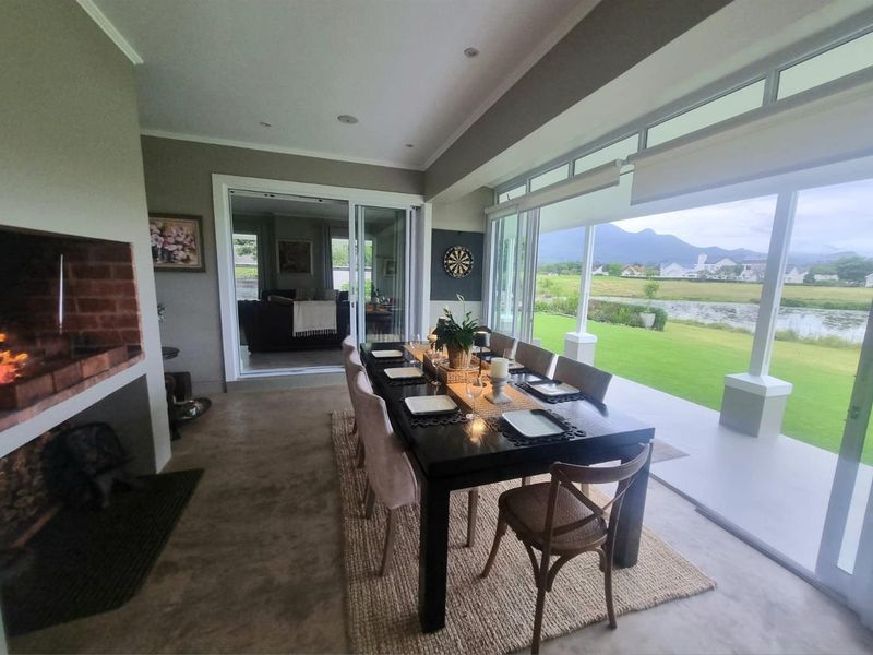 Spacious dining area featuring a built-in brick fireplace, polished concrete flooring, and large sliding glass doors opening onto a scenic garden and pond view.