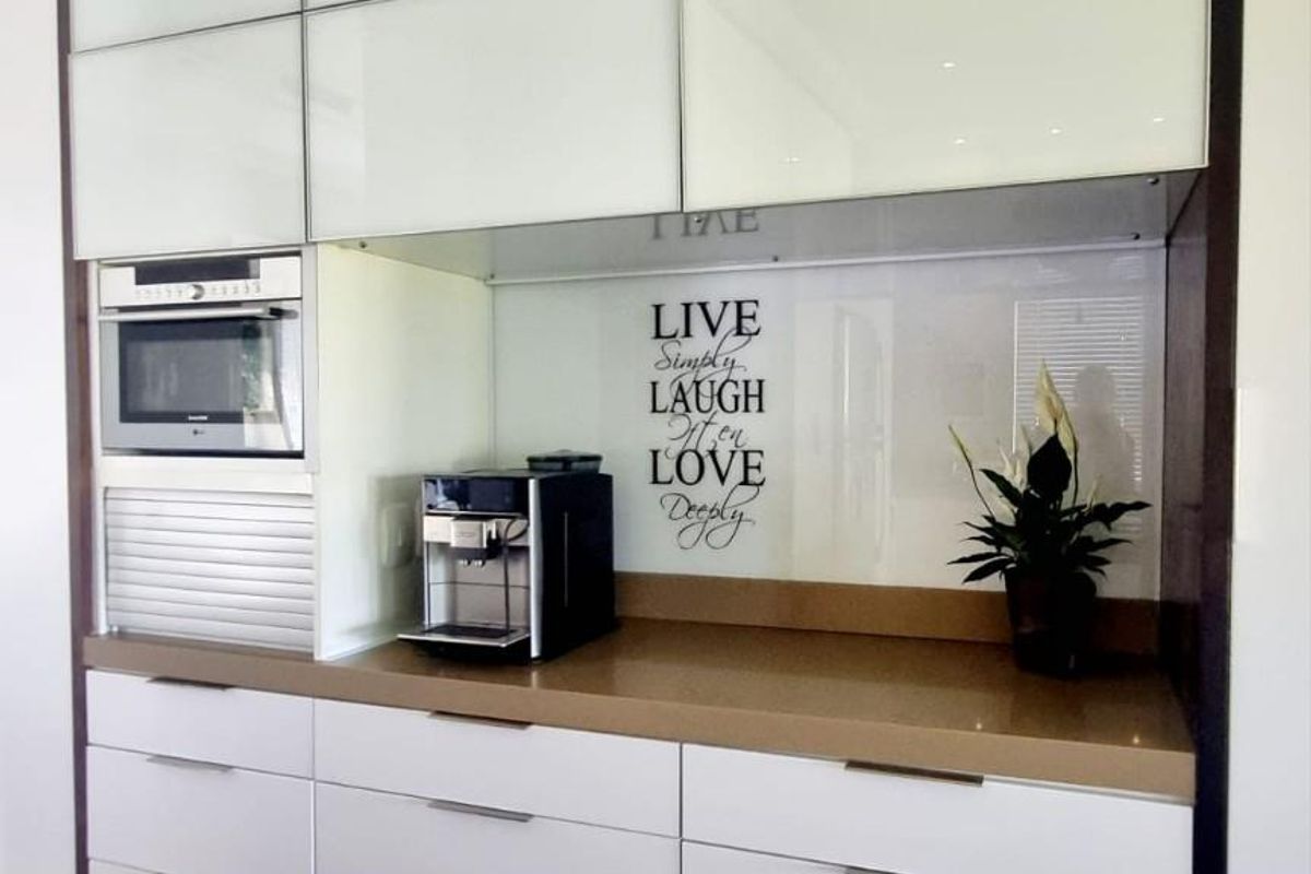 Modern kitchen cabinetry featuring high-gloss white doors, integrated microwave, stone countertop, and a glass splashback.