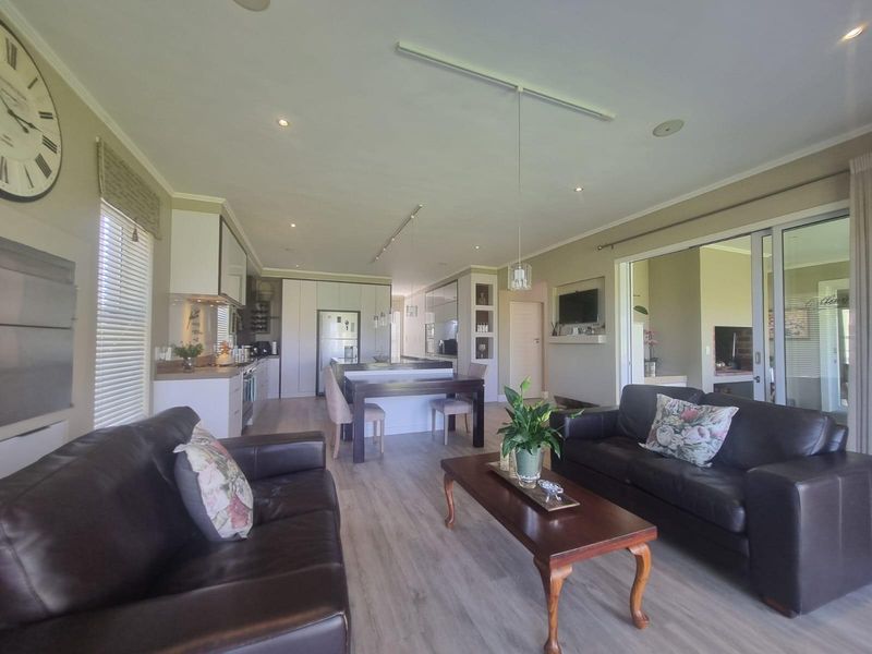 Open-plan living area featuring a modern kitchen with built-in cabinetry, light wood-look flooring, and seamless flow to an adjacent patio through sliding glass doors.
