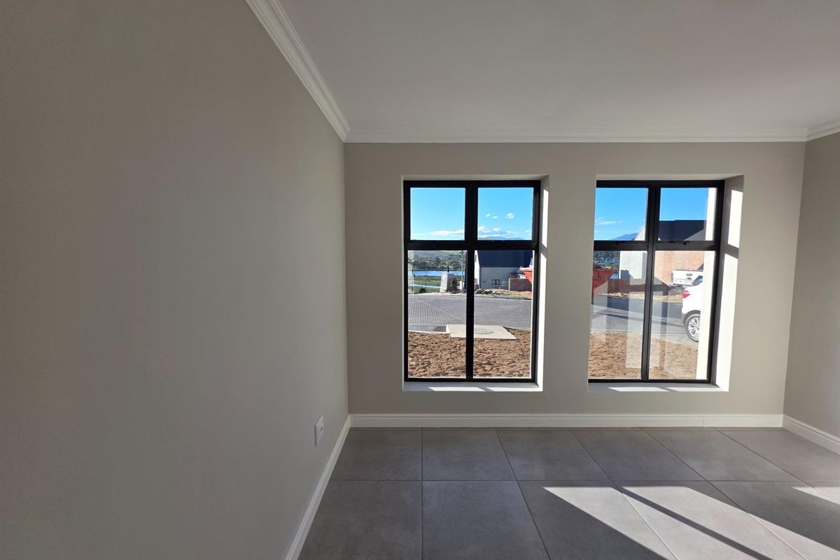 A bright, modern living area featuring neutral wall tones, large black-framed windows, and sleek tiled flooring, offering a clean and contemporary aesthetic.