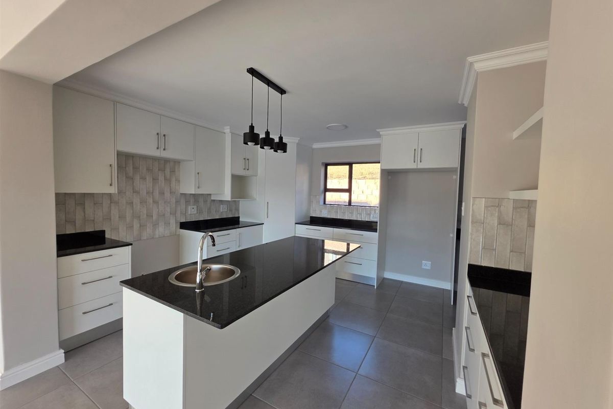 Modern kitchen featuring a central island with a sink, granite countertops, white cabinetry, and tiled backsplash.
