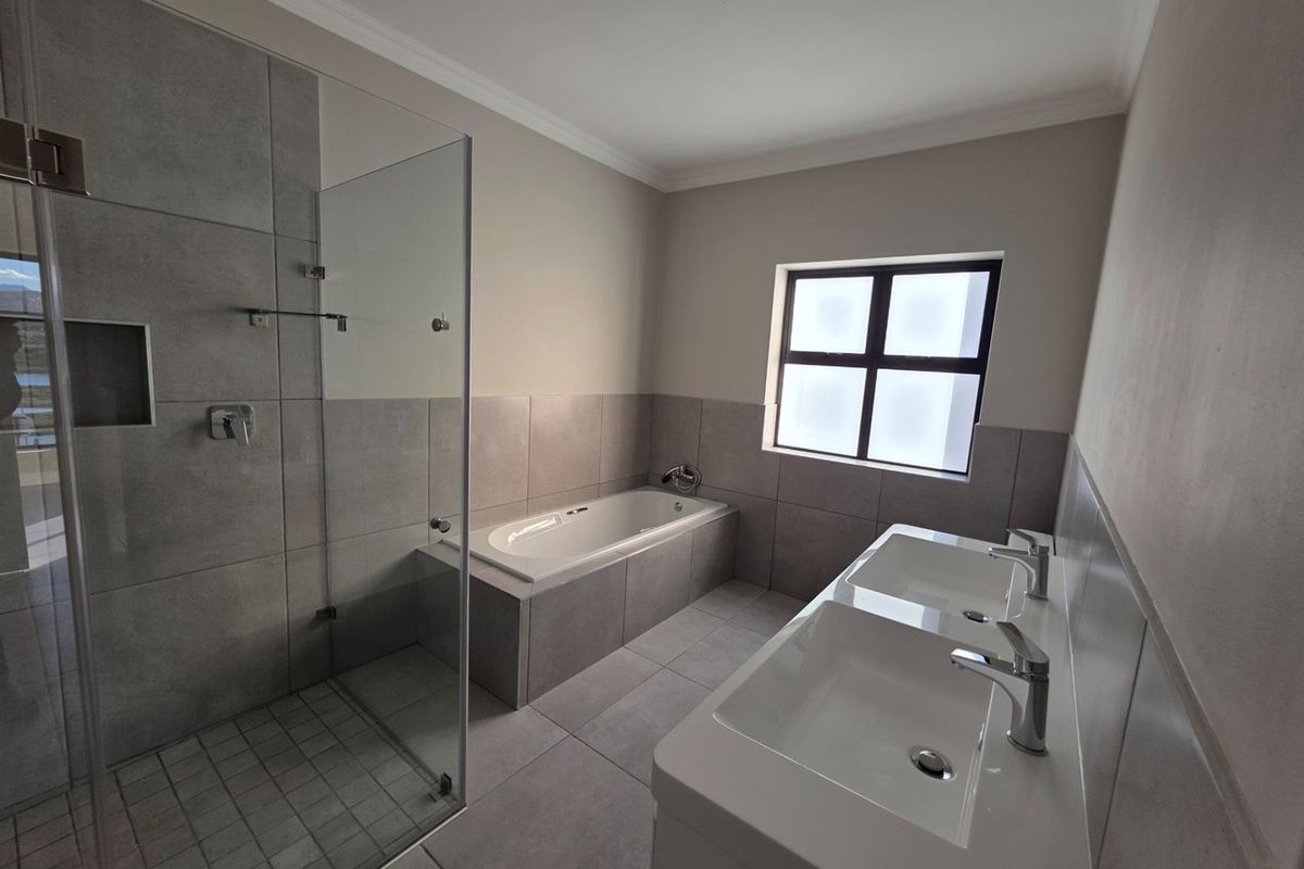 Modern bathroom featuring a double vanity, a built-in bathtub, and a glass-enclosed walk-in shower with neutral grey tiling throughout.
