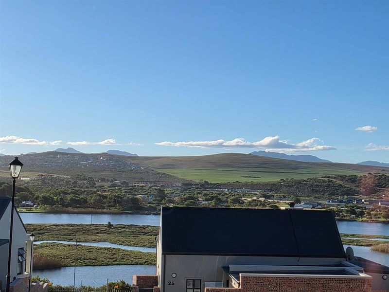 A scenic elevated view overlooking a river, surrounding wetlands, and distant rolling hills under a clear blue sky.