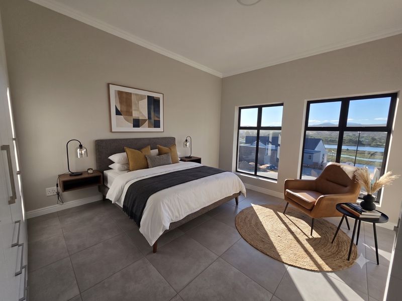 A modern, well-lit bedroom featuring large windows with scenic views, neutral tiled flooring, and built-in storage.