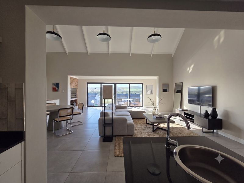 Spacious open-plan living area featuring vaulted ceilings with exposed beams, tiled flooring, a built-in fireplace, and seamless flow to an outdoor patio.