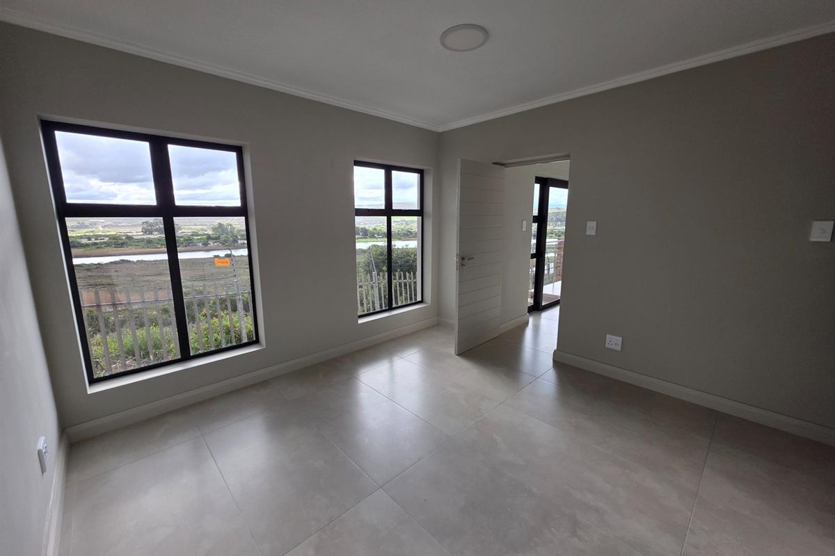 A bright, empty bedroom featuring neutral tiled flooring, modern black-framed windows with scenic views, and a clean, minimalist interior finish.