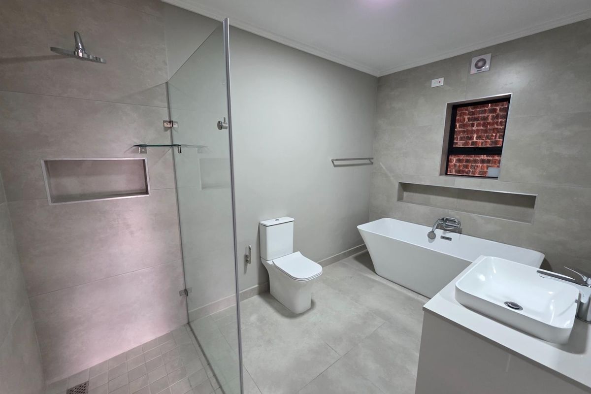 Modern bathroom featuring a walk-in glass shower, freestanding bathtub, contemporary vanity, and neutral large-format floor and wall tiling.
