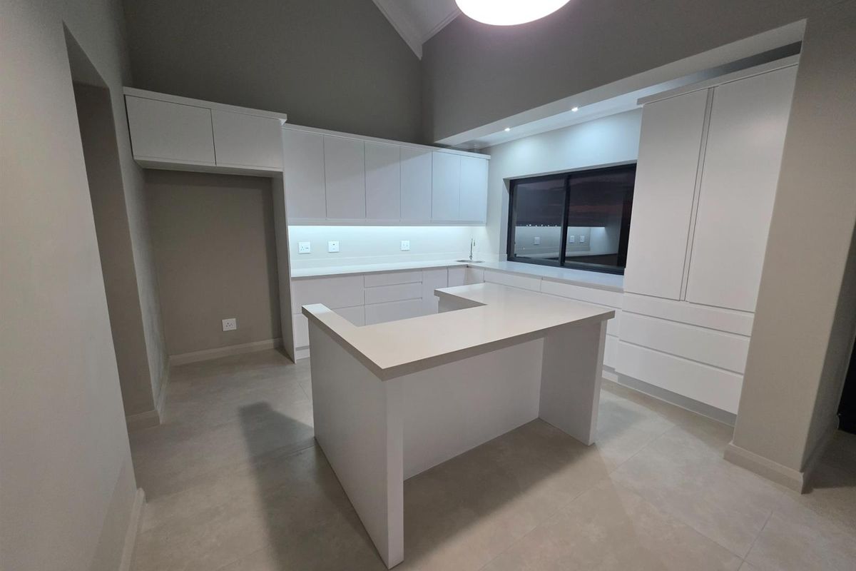 Modern kitchen featuring white cabinetry, stone countertops, a central island, and high vaulted ceilings with integrated lighting.