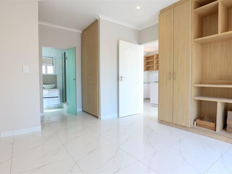 A bright, modern bedroom featuring sleek marble-look floor tiles, ample built-in cupboard space, and direct access to an en-suite bathroom.