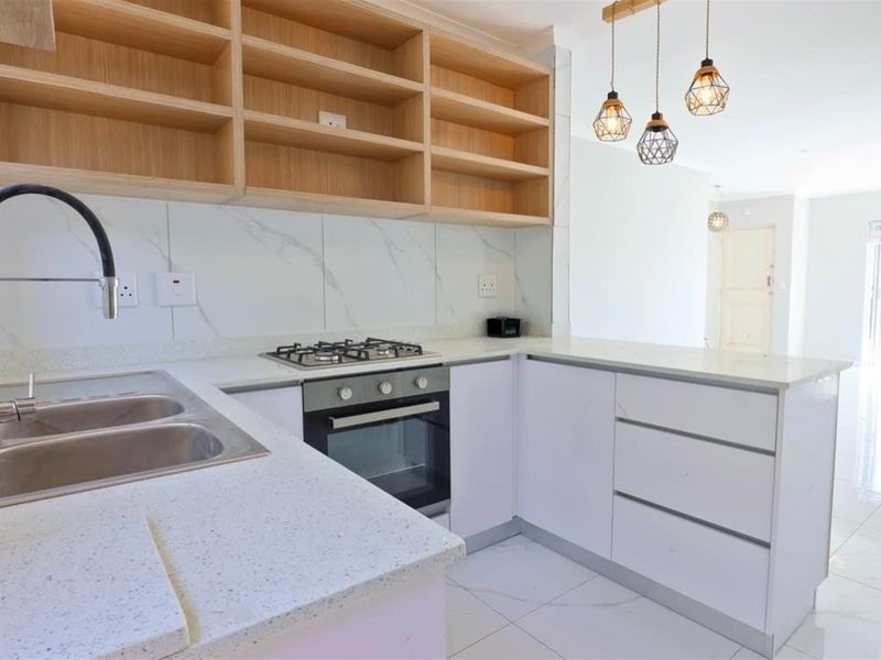 Modern kitchen featuring white cabinetry, stone countertops, marble-look backsplash, built-in gas cooktop, oven, and stylish pendant lighting.
