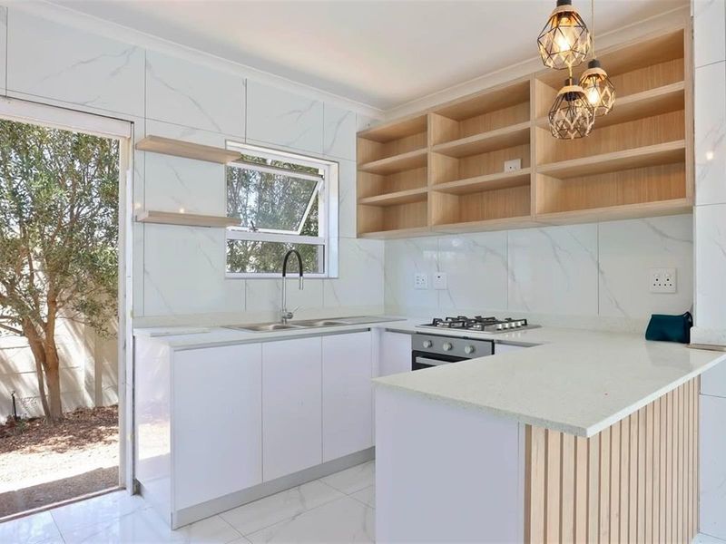 Modern kitchen featuring white cabinetry, stone countertops, gas hob, built-in oven, and marble-look wall tiles with direct access to the garden.