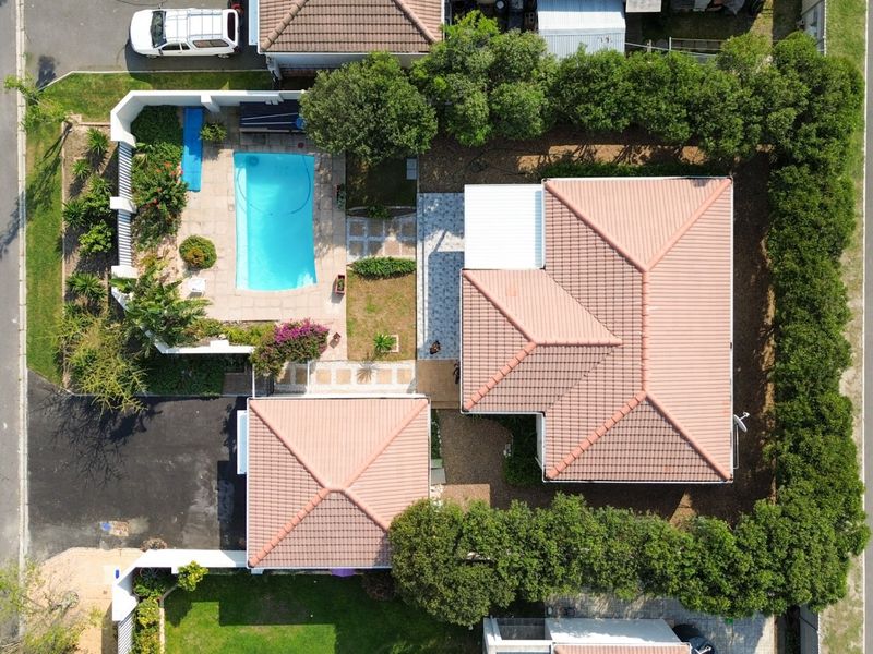 Aerial view of the property featuring a tiled roof house, a swimming pool, paved patio areas, and established garden landscaping.