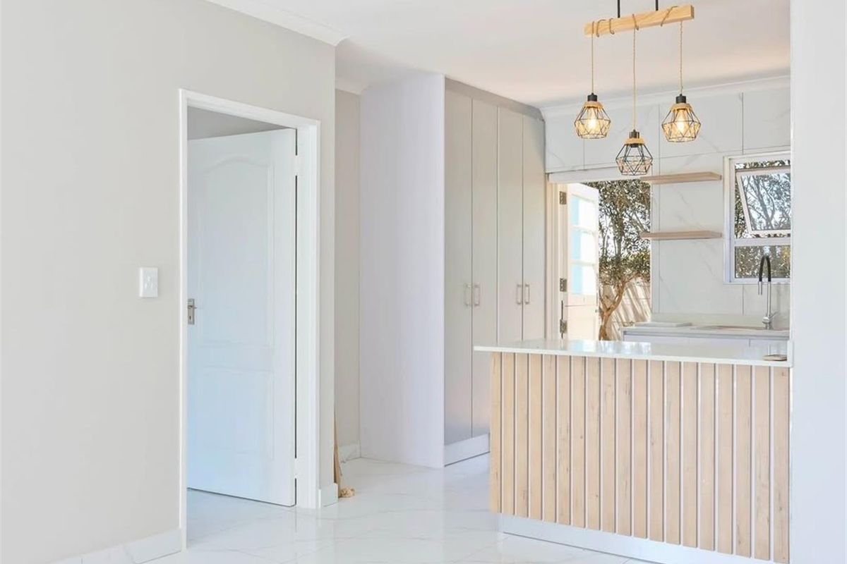 Modern kitchen featuring a timber-slatted island, marble-look splashback, sleek built-in cabinetry, and stylish pendant lighting, opening to an outdoor area.