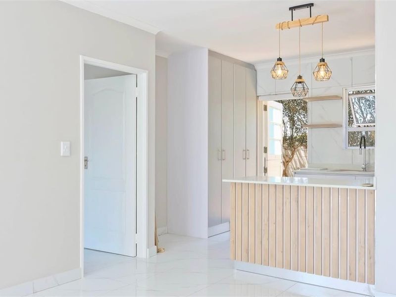 Modern kitchen featuring a timber-slatted island, marble-look splashback, sleek built-in cabinetry, and stylish pendant lighting, opening to an outdoor area.