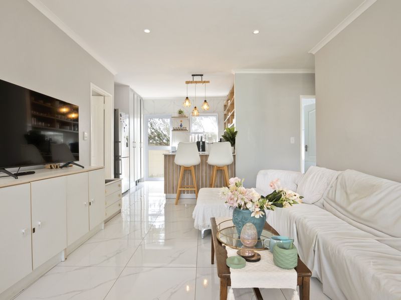 Bright open-plan living and kitchen area featuring modern porcelain tile flooring, recessed lighting, and a functional kitchen island with pendant lights.