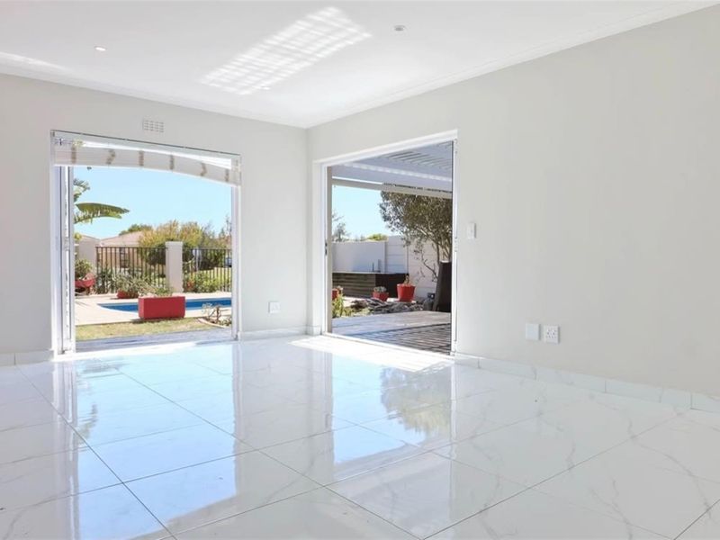 Bright and spacious living area featuring polished porcelain tile flooring, recessed lighting, and dual sliding glass doors providing direct access to the outdoor pool area.