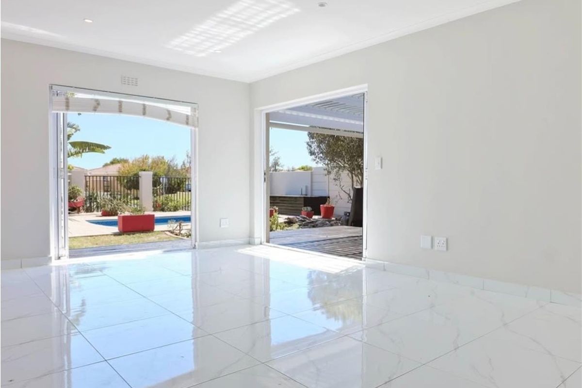 Bright and spacious living area featuring polished porcelain tile flooring, recessed lighting, and dual sliding glass doors providing direct access to the outdoor pool area.