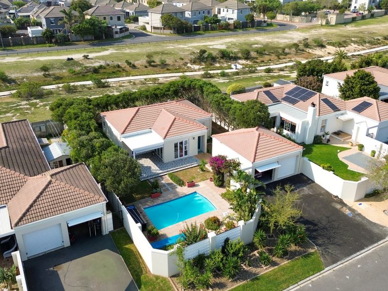 Aerial view of a residential property featuring a swimming pool, tiled roof, solar panels, and a private driveway within a suburban estate.