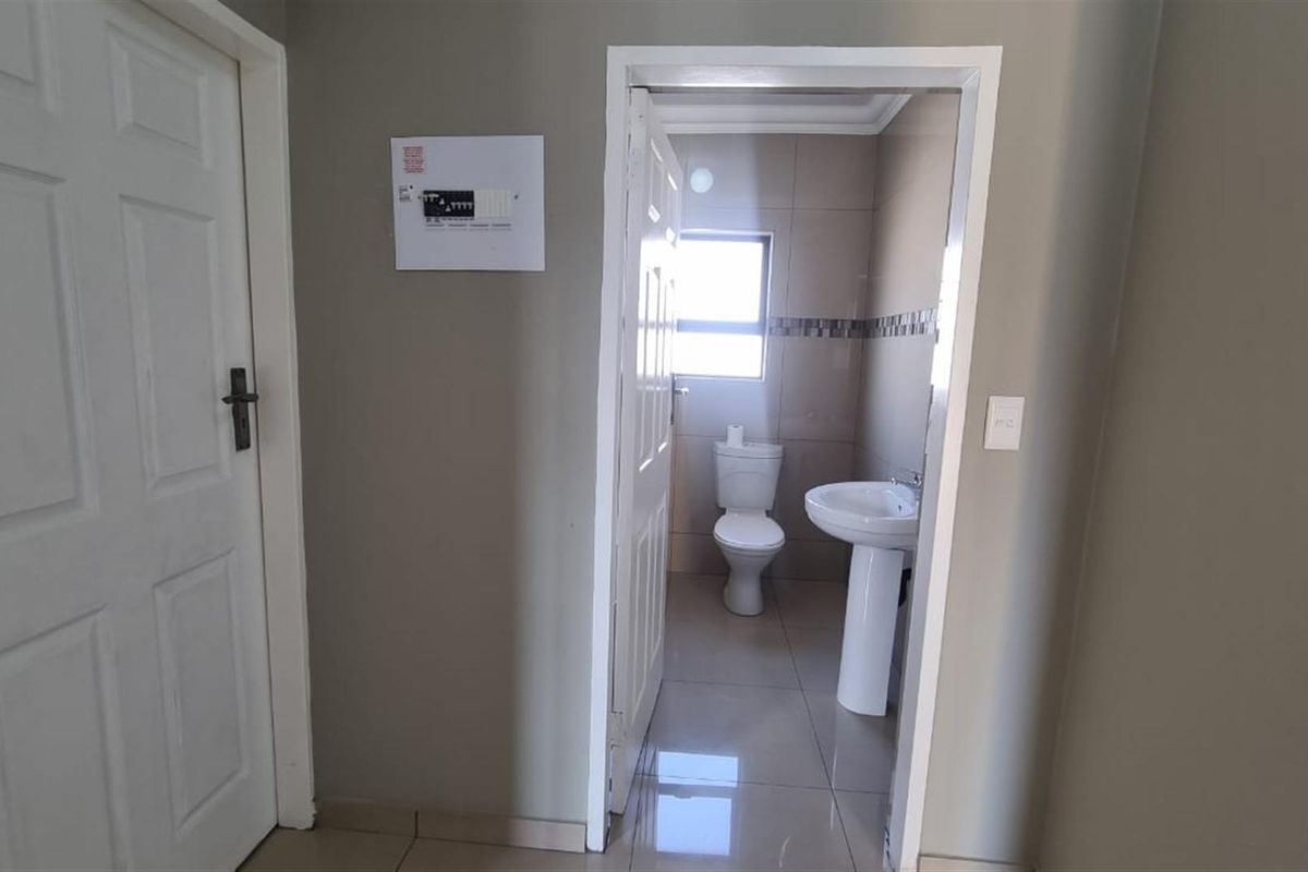 A view from a hallway into a functional bathroom featuring a pedestal basin, toilet, and tiled flooring.