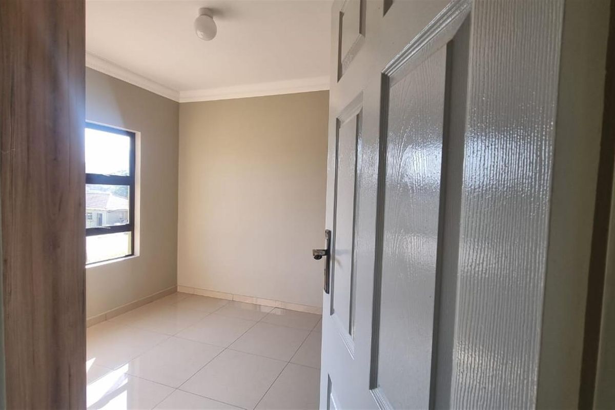 A bright, empty bedroom featuring neutral wall paint, tiled flooring, and a modern window, viewed from the doorway.