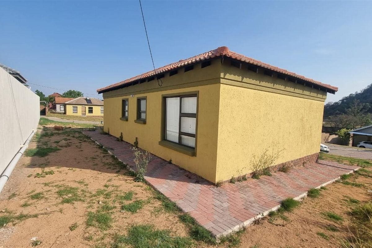 A view of the side and rear exterior of the house, featuring a paved walkway, textured yellow facade, and tiled roof.