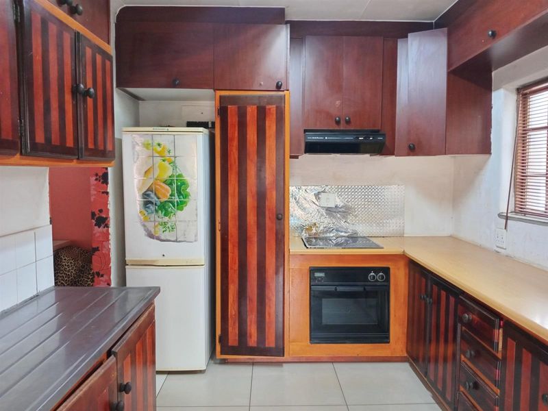 A functional kitchen featuring dark wood-toned cabinetry, built-in oven and hob, and tiled flooring, offering potential for a modern cosmetic update.