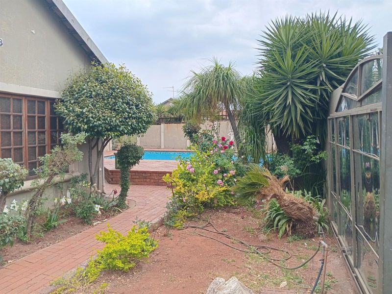 A private backyard featuring a swimming pool, brick-paved pathways, and established garden landscaping with mature trees and shrubs.
