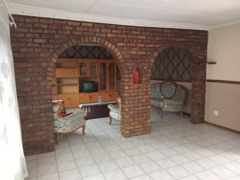 Living area featuring distinctive exposed brick archways, ceramic tiled flooring, and decorative ceiling cornicing, offering a dated aesthetic ready for modernization.