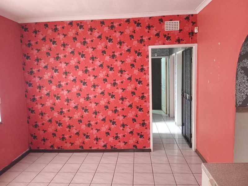 An empty living area featuring ceramic floor tiles, a security gate, and dated floral wallpaper, offering a blank canvas for renovation.