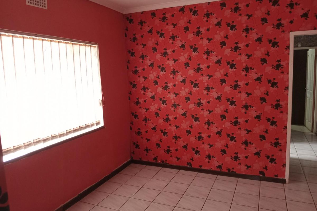 An empty bedroom featuring tiled flooring, a window with vertical blinds, and a prominent floral wallpaper feature wall.