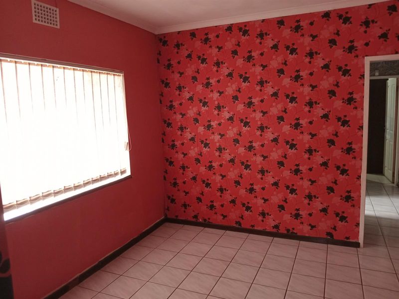 An empty bedroom featuring tiled flooring, a window with vertical blinds, and a prominent floral wallpaper feature wall.