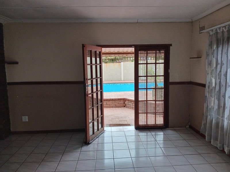 Empty living room featuring tiled flooring and wooden french doors opening onto a patio and swimming pool area.