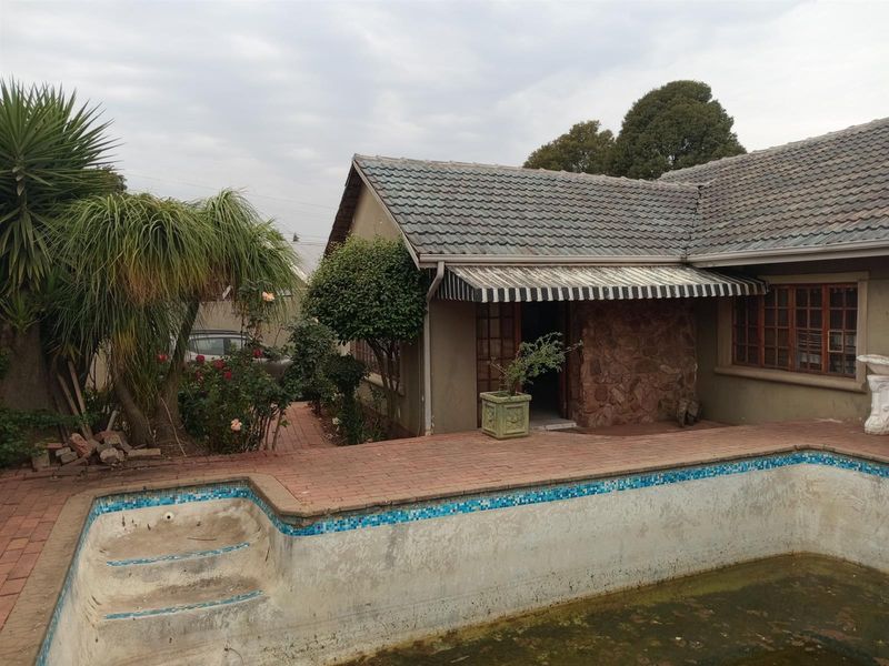 Exterior view of a house featuring a swimming pool with a brick paved patio, stone cladding detail, and a retractable awning over the entrance.