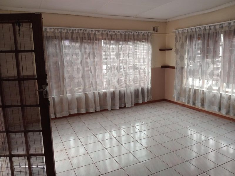 An empty living room featuring tiled flooring, timber framed door, and built-in shelving, offering a blank canvas for renovation.