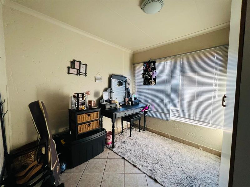 A bedroom featuring tiled flooring, textured walls, and a large window fitted with horizontal blinds, providing natural light to the space.