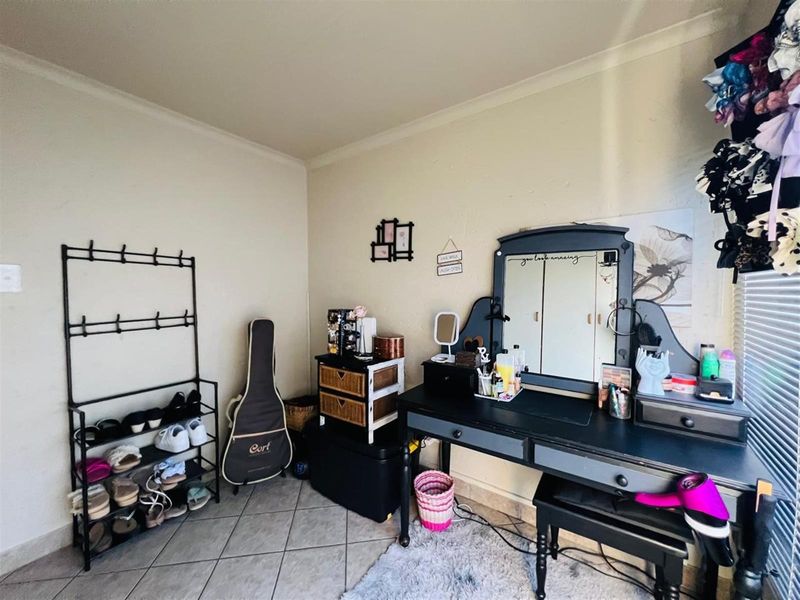 A bedroom space featuring tiled flooring and neutral wall finishes, currently utilized as a dressing area.