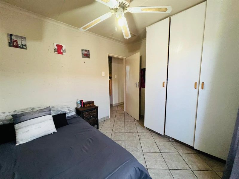 A bedroom featuring built-in cupboards, tiled flooring, and a ceiling fan, providing a functional living space.