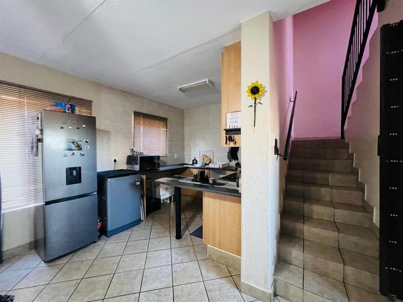 A functional kitchen area featuring built-in cabinetry and tiled flooring, adjacent to an internal staircase with a metal handrail.
