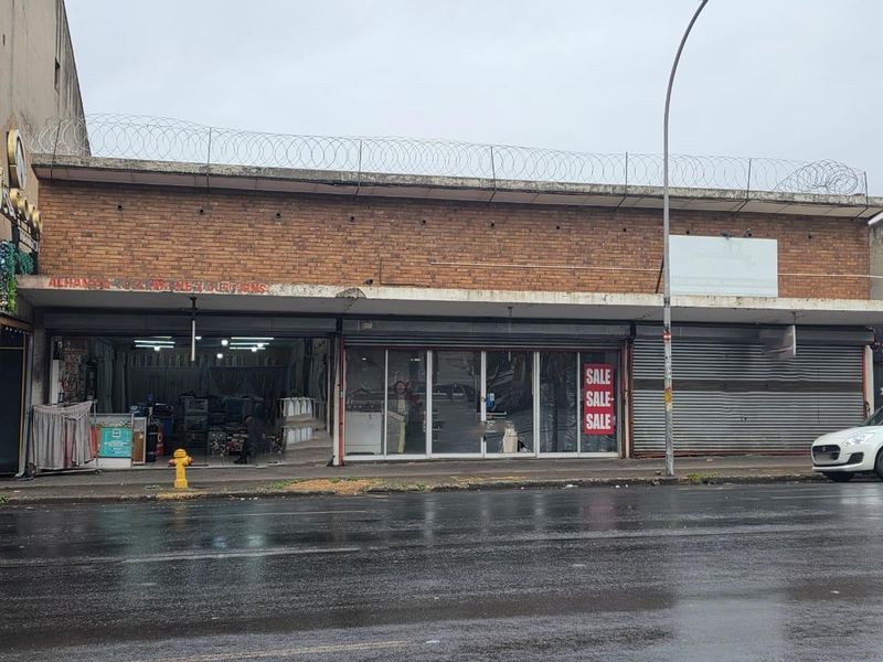 Commercial storefront featuring a brick facade, large glass display windows, and secure roller shutter doors, located along a street front.