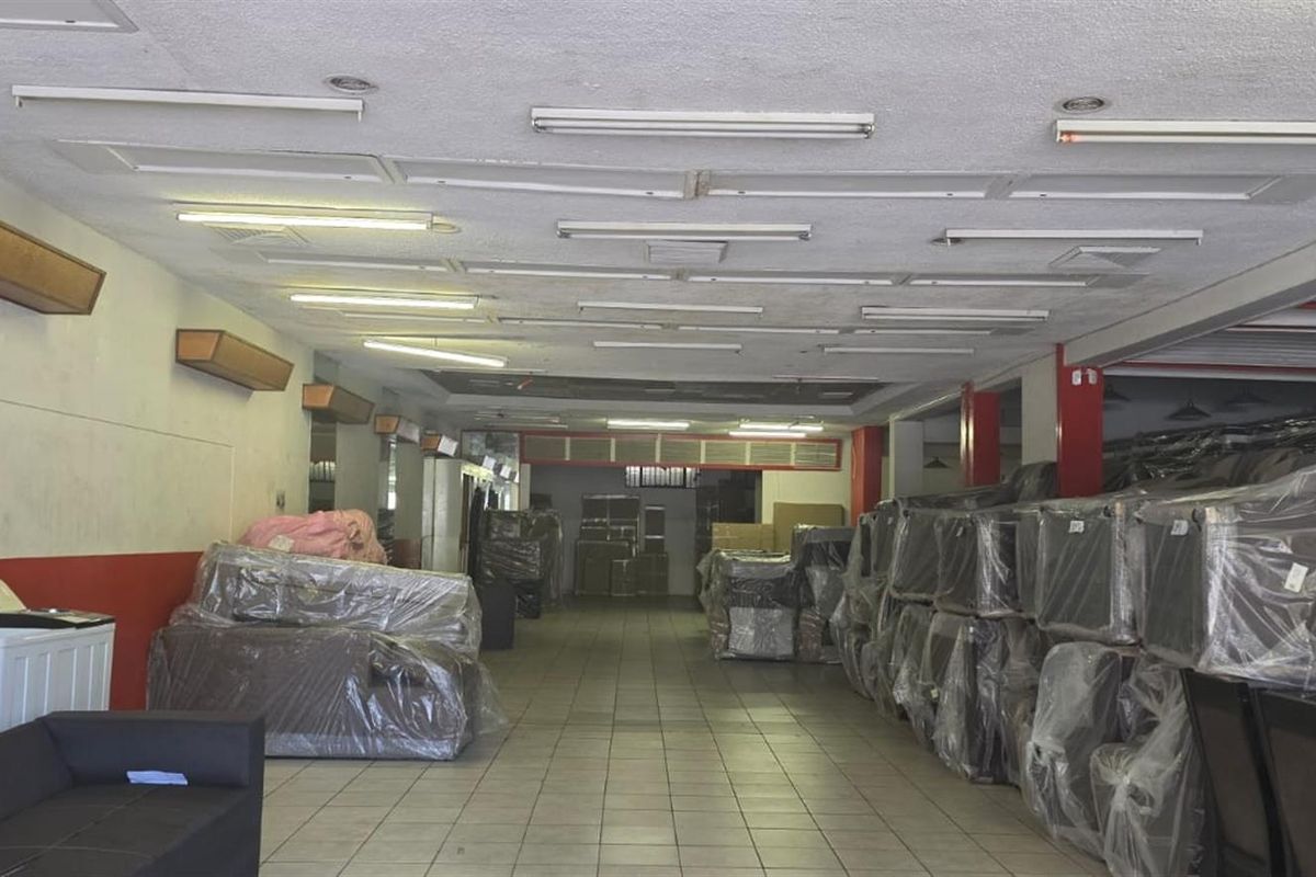 Spacious commercial open-plan area featuring tiled flooring, fluorescent lighting, and wall-mounted air conditioning units, suitable for retail or showroom use.