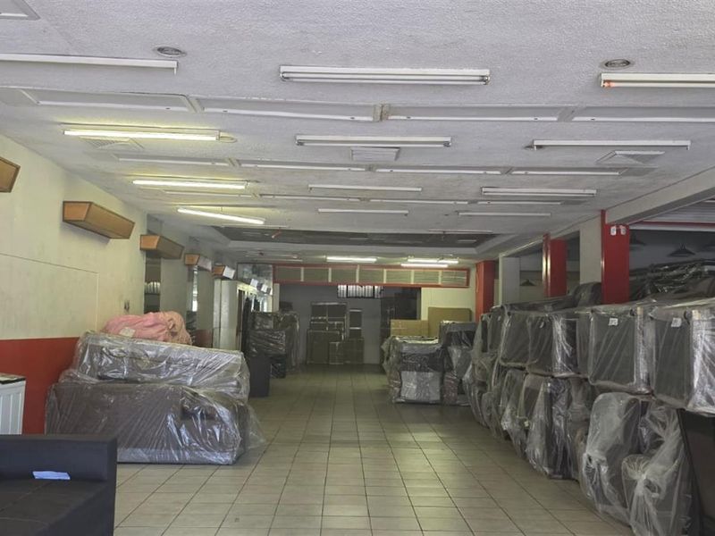 Spacious commercial open-plan area featuring tiled flooring, fluorescent lighting, and wall-mounted air conditioning units, suitable for retail or showroom use.