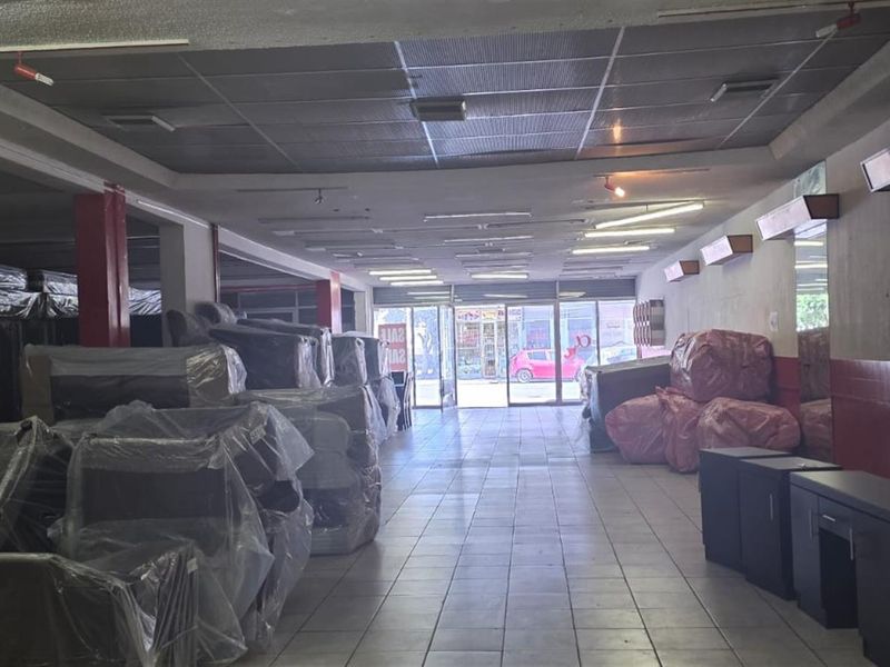 Spacious commercial open-plan retail area featuring tiled flooring, suspended ceilings, and a glass storefront entrance, suitable for various business applications.