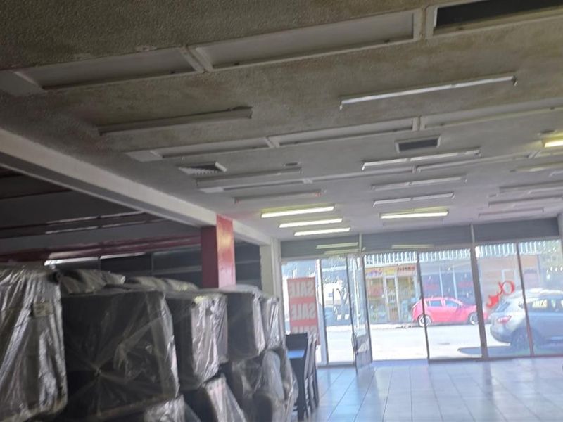 Open plan commercial retail space featuring tiled flooring, extensive glass storefront frontage, and integrated fluorescent lighting throughout the ceiling.