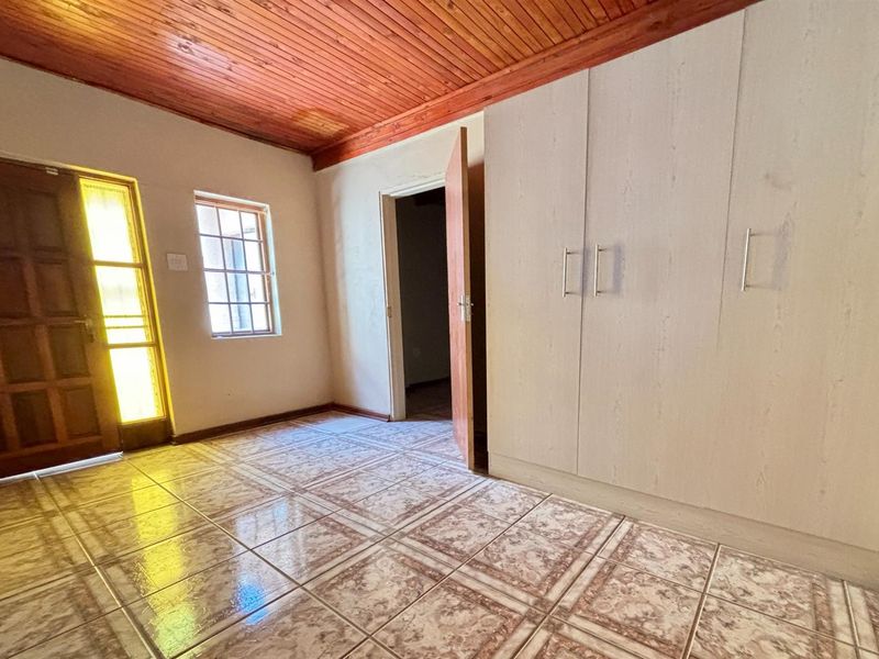 An empty bedroom featuring built-in cupboards, tiled flooring, and a traditional wooden ceiling.