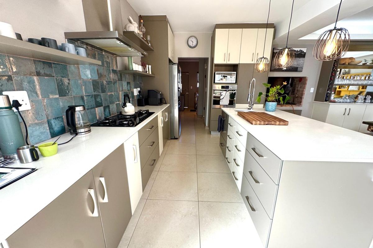 Modern kitchen featuring a central island, stone countertops, gas hob, built-in oven, and stylish tiled backsplash with ample cabinetry.