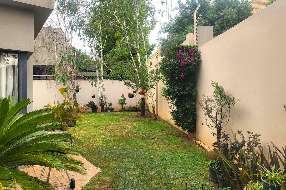 A private rear garden featuring a lawn area, established trees, and high perimeter walls with integrated electric fencing for added security.